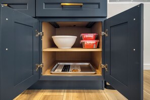 A kitchen cabinet with open doors, containing a white bowl, two red containers, and a baking tray. - Charming Atwater Village Retreat 2BR + 2BA (Los Angeles)