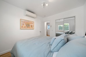 A bedroom with a large bed, a painting on the wall, an air conditioning unit, and a sliding door leading to another room. - Charming Atwater Village Retreat 2BR + 2BA (Los Angeles)