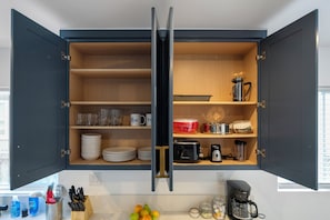 A kitchen with open cabinets, containing plates, glasses, a coffee maker, and a toaster. - Charming Atwater Village Retreat 2BR + 2BA (Los Angeles)