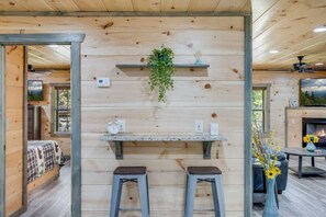 Ein Holzinterieur mit Barbereich, zwei Barhocker, einer hängenden Pflanze und einem Kamin.