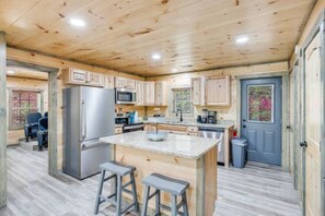 A spacious kitchen with wooden cabinets, a central island, bar stools, and a refrigerator. - Cozy Cub Cabin - Movie Room, Games, & Hot Tub! (Gatlinburg)