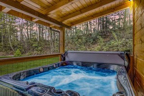 A hot tub with a wooden deck and a view of a forested area. - Cozy Cub Cabin - Movie Room, Games, & Hot Tub! (Gatlinburg)