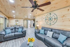 A modern interior with a ceiling fan, two grey leather sofas, a round mirror, and a wall with a circular design. - Cozy Cub Cabin - Movie Room, Games, & Hot Tub! (Gatlinburg)