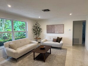 A modern living room with two sofas, a coffee table, a decorative plant, and a large window with a view of greenery. - Beach, Golf, & Fitness Getaway, Newly Renovated. (Naples)