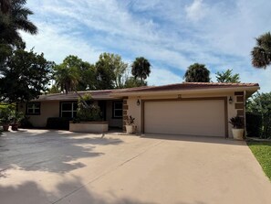 A residential house with a garage, a driveway, and surrounding greenery. - Beach, Golf, & Fitness Getaway, Newly Renovated. (Naples)