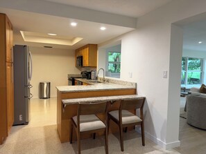 A kitchen with a granite countertop, wooden cabinets, and a stainless steel refrigerator. - Beach, Golf, & Fitness Getaway, Newly Renovated. (Naples)