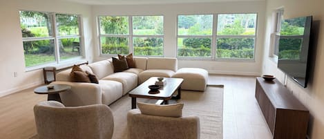 Una sala de estar moderna con un sofá modular, otomanas redondas, una mesa de centro y un televisor de pantalla plana.