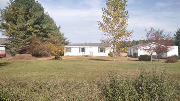 A single-story house with a front yard, surrounded by trees and a grassy field.