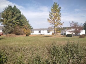 A single-story house with a front yard, surrounded by trees and a grassy field.