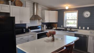 A kitchen with white cabinets, a black refrigerator, a stainless steel range hood, and a window with a clock.