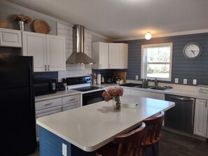A kitchen with white cabinets, a black refrigerator, a stainless steel range hood, and a window with a clock.