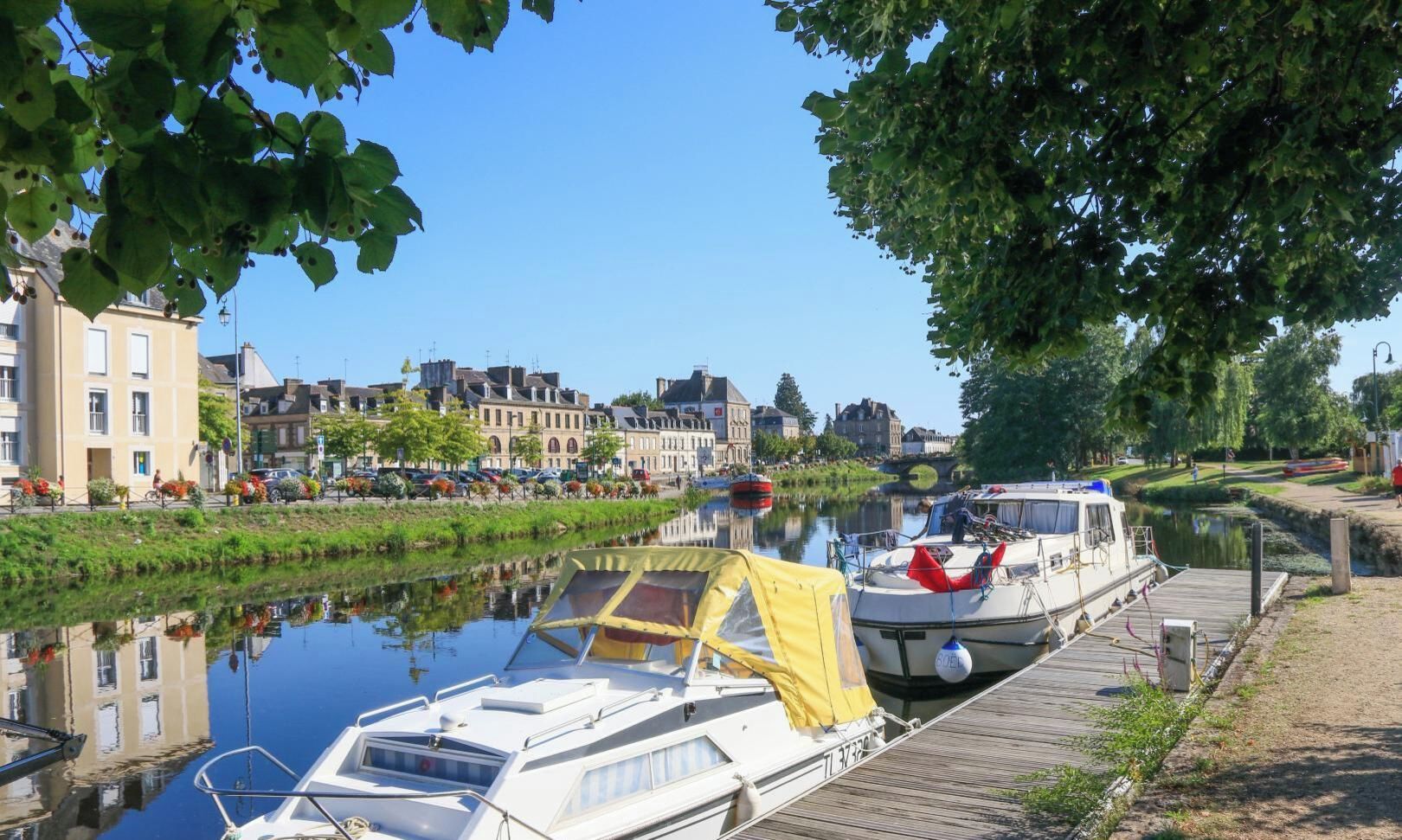 Un canal bordé de bateaux amarrés, une promenade en bois et des bâtiments en arrière-plan.