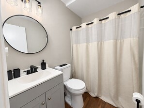 A bathroom with a round mirror, a white sink, a toilet, and a shower curtain. - Pleasant Queen Room & Private Bathroom in Rocky Mount (Rocky Mount)