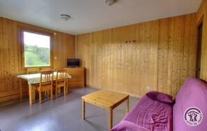 Ett rum med träväggar, ett matbord med stolar, en soffa och en tv.