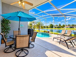 A covered outdoor area with a pool, lounge chairs, and a table with chairs. - Perfect pool house with waterfront for the best Disney experience in Kissimmee. (Kissimmee)
