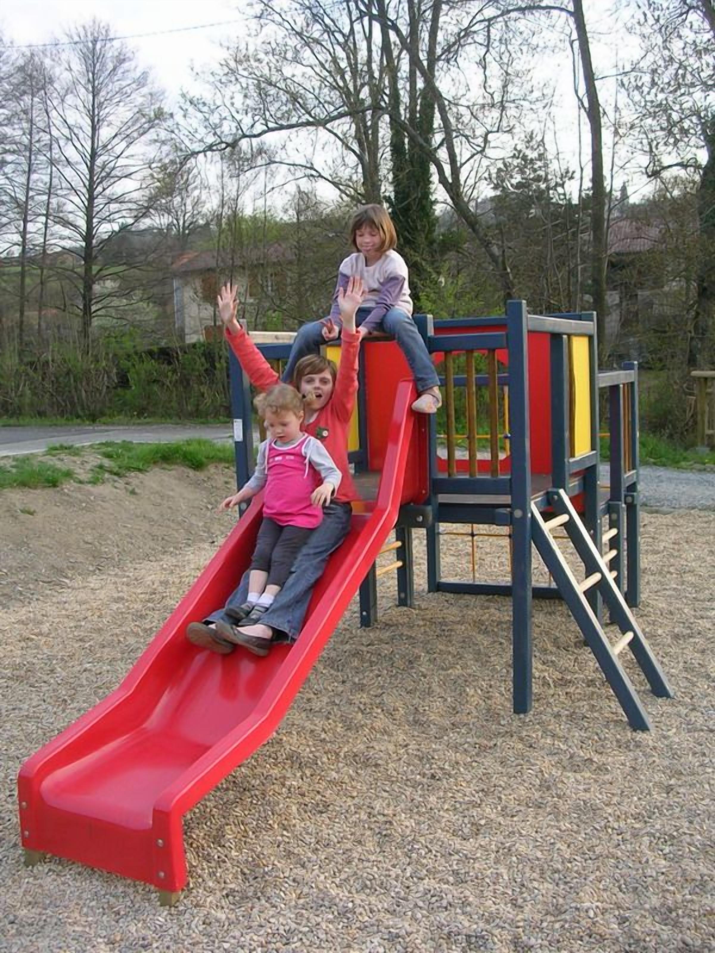 Un parque infantil con un tobogán rojo y una estructura para escalar.