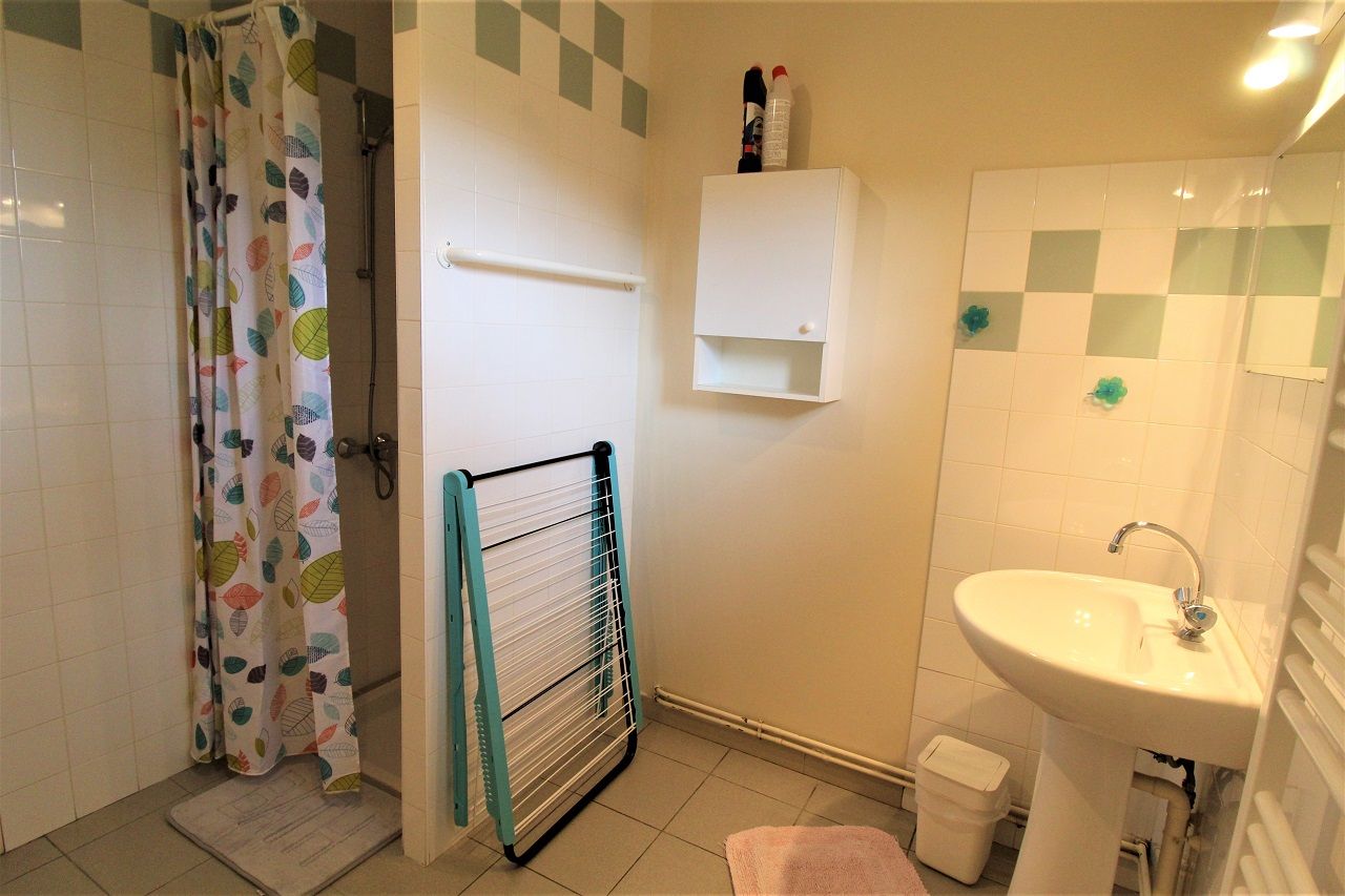 A bathroom with a shower curtain, a drying rack, a sink, and a small cabinet.