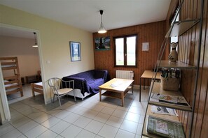 Een kleine, gezellige kamer met een bed, een stoel, een tafel en een plank met spullen.