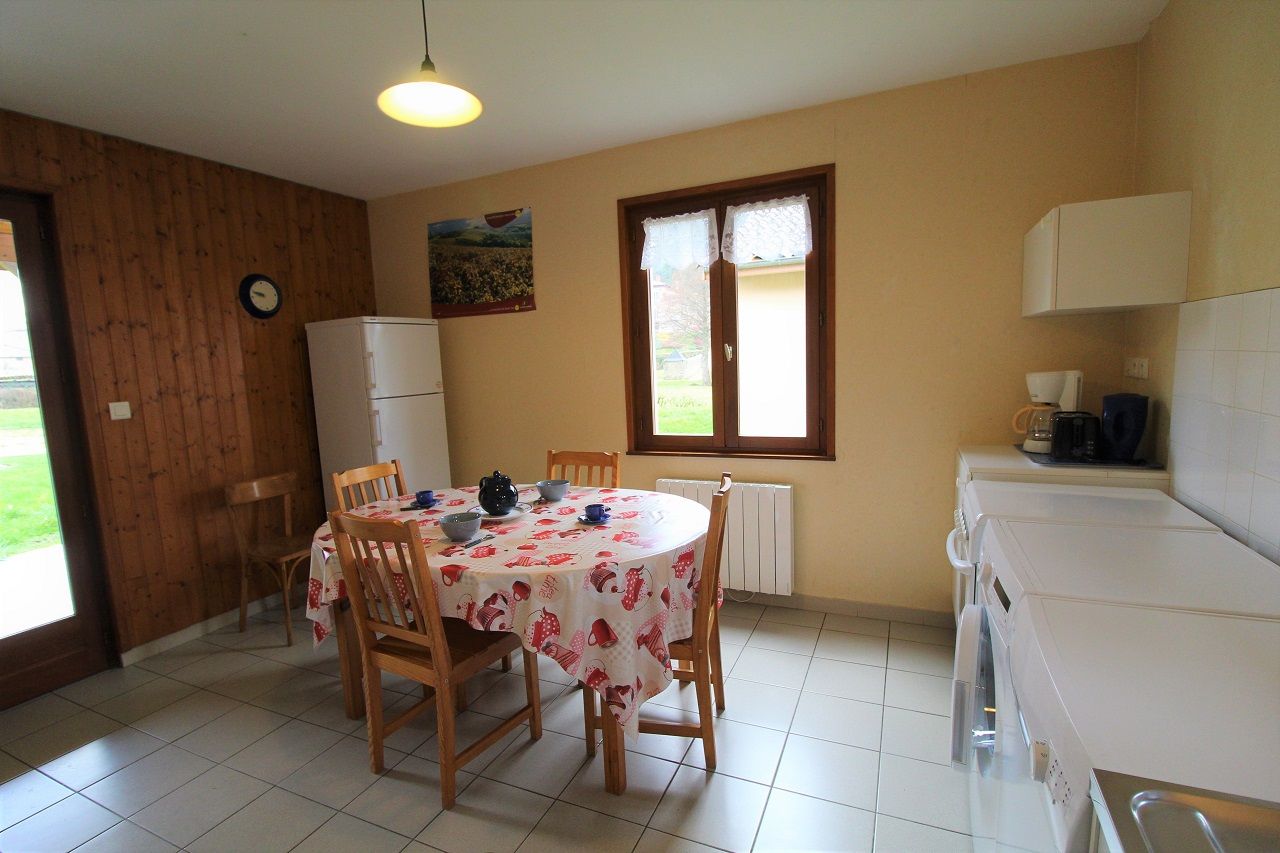 A kitchen with a dining table, chairs, a refrigerator, a window with curtains, and a washing machine.