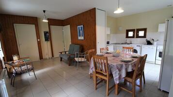 A dining area with a table set for four, a kitchen with appliances, and a wooden wall.