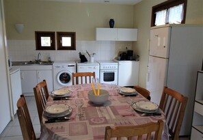 Una cocina compacta con una mesa de comedor preparada para cuatro personas, una lavadora, una estufa y un refrigerador.