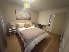 A bedroom with a bed, bedside tables, a desk, a chair, a hanging light fixture, and a door. - Cosy & Modern 2 bed house |Close to City Centre| Driveway (Nottingham)