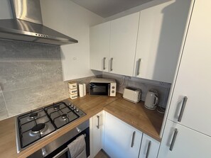 A modern kitchen with a gas stove, a built-in oven, white cabinets, a stainless steel range hood, and a wooden countertop. - Cosy & Modern 2 bed house |Close to City Centre| Driveway (Nottingham)
