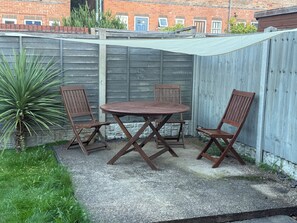 Un patio con una mesa, cuatro sillas, una valla de madera y una planta.