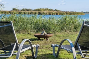 Two lounge chairs facing a body of water with a fire pit in the center. - Cozy holiday home with private jetty (Randers NØ)