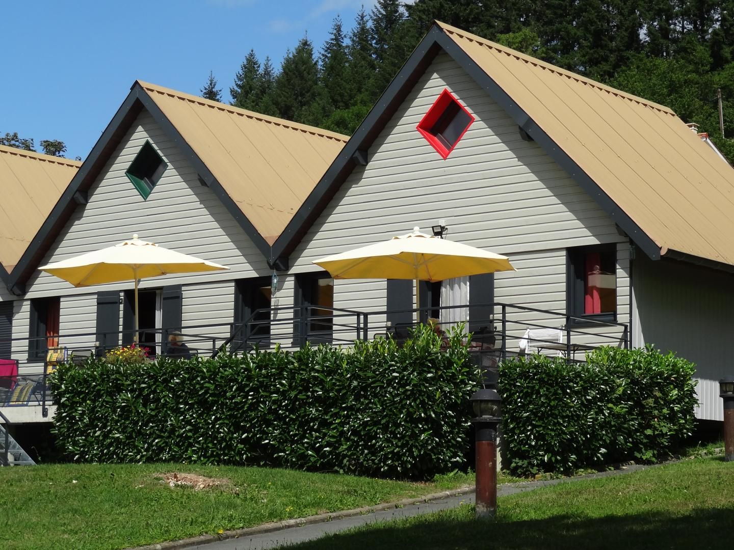 A row of three-story buildings with a flat roof, each with a balcony and a red window.