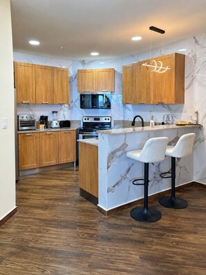 Eine moderne Küche mit Holzschränken, einem eingebauten Ofen, einer Mikrowelle und einer Bar mit Hockern.