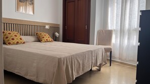 Quarto com cama, cadeira, guarda-roupa, porta e janela com cortinas.
