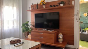 Een moderne woonkamer met een flatscreen televisie bevestigd aan een houten kast, een glazen salontafel en een potplant.