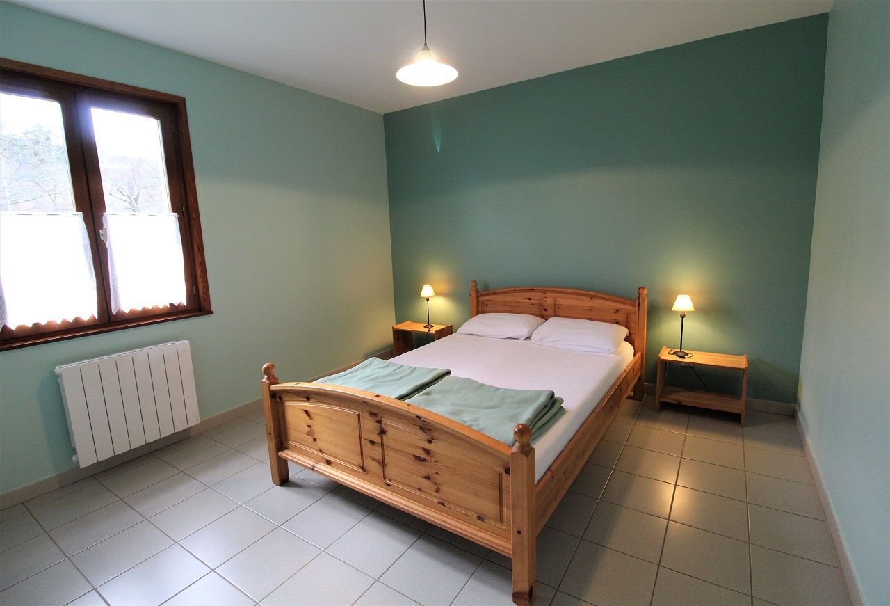 Un dormitorio con una cama de madera, dos mesitas de noche con lámparas, un radiador y una ventana con persianas.