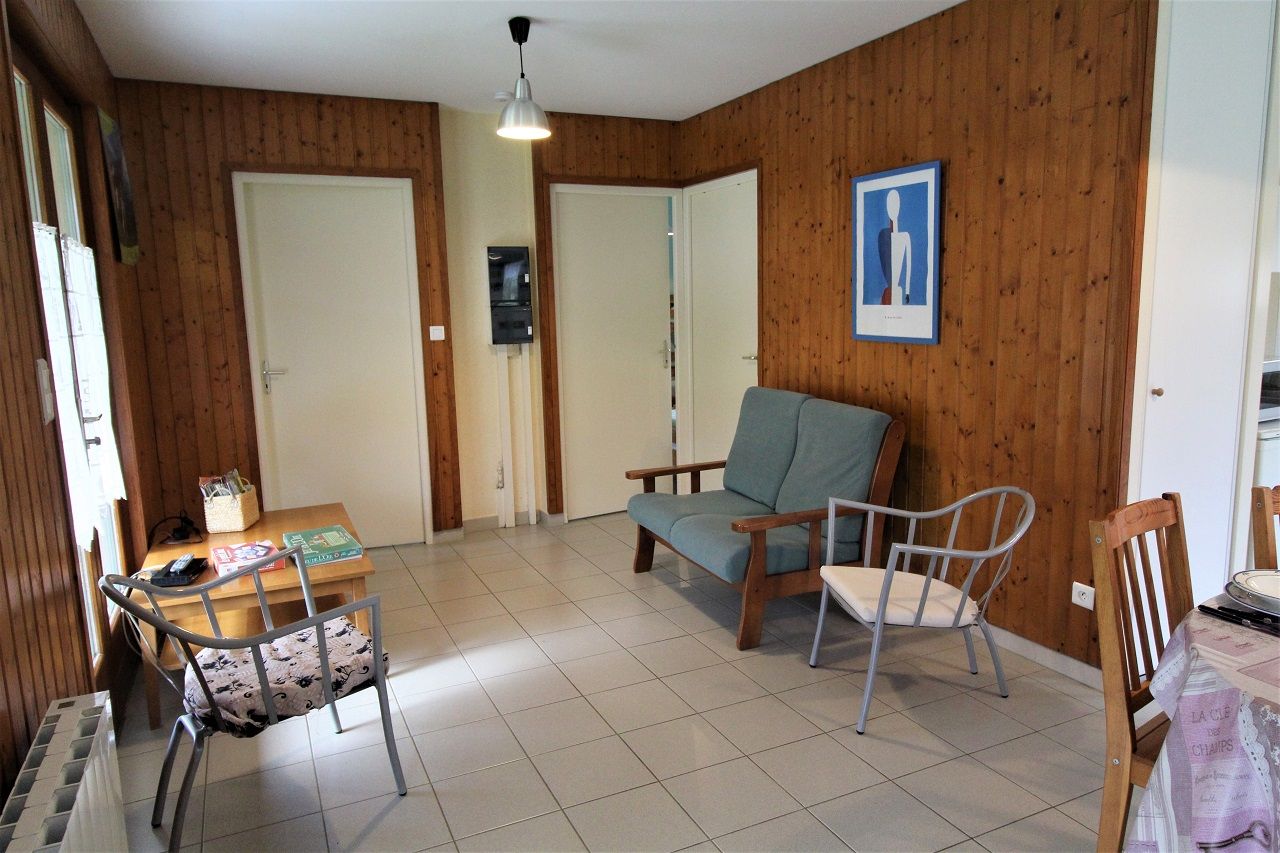 A room with wooden walls, a dining table with chairs, a sofa, and a framed picture on the wall.