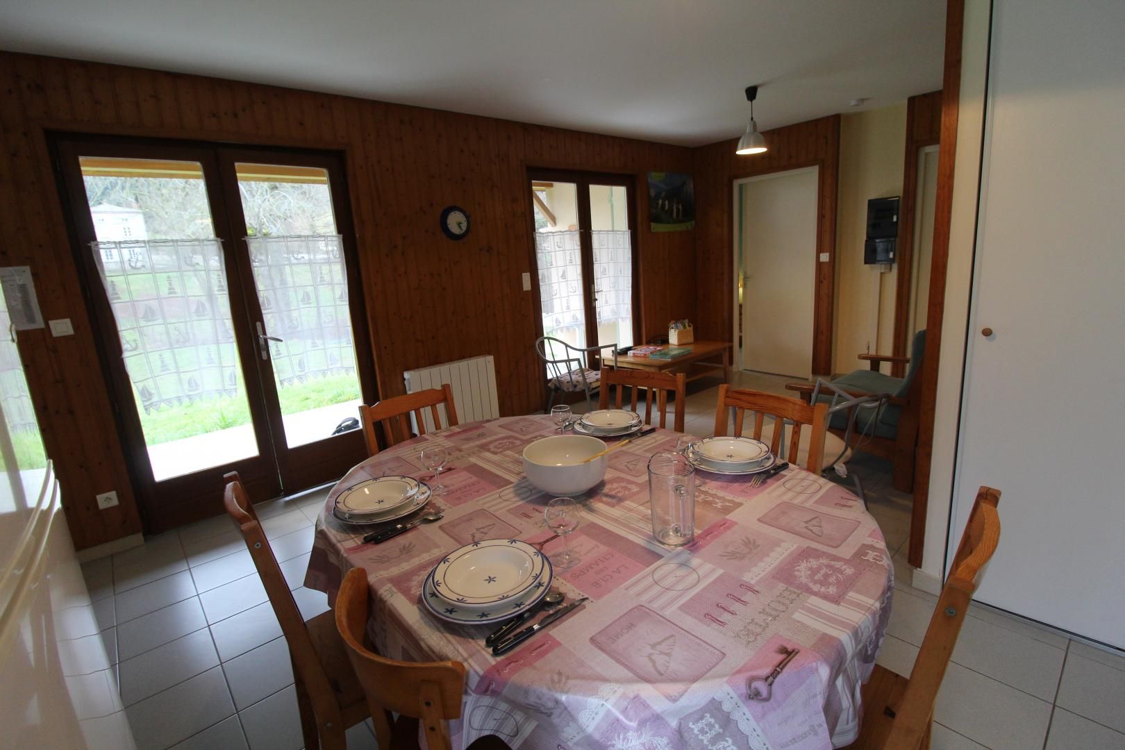 A dining room with a round table set for six, wooden chairs, a large bowl, plates, cutlery, and a vase.