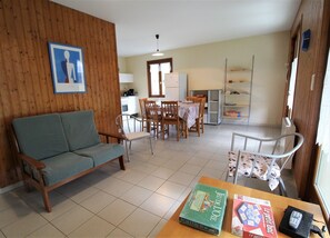 Een woonkamer met een bank, een eettafel, stoelen en een keukenhoek met een koelkast en kasten.