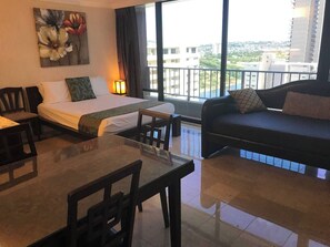 Une chambre d’hôtel comprenant un lit, un canapé, une table à manger et offrant une vue sur la ville grâce à de grandes fenêtres.