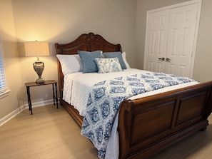 A bedroom with a wooden bed, a bedside table with a lamp, and a door in the background. - Perfect 3-bedroom house in beautiful Memphis for your stay (Memphis)
