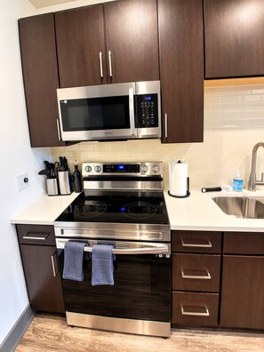 A modern kitchen with dark wood cabinets, stainless steel appliances, and a white countertop. - Stadium Stay | Rooftop Lounge + Fitness Center (Atlanta)