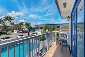A balcony with a view of a swimming pool, a street with cars, and a building with a blue roof. - Sunny 1 Bed 1 Bath Apt Minutes to the Sea, Pool (Lauderdale-by-the-Sea)