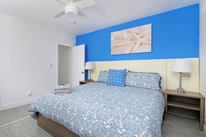 A bedroom with a bed, nightstands, a ceiling fan, and a wall-mounted artwork. - Sunny 1 Bed 1 Bath Apt Minutes to the Sea, Pool (Lauderdale-by-the-Sea)