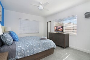 Ein Schlafzimmer mit einem Bett, einem Schminktisch, einem Deckenventilator und zwei Fenstern mit Jalousien.