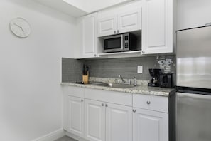 A kitchen with white cabinets, a stainless steel refrigerator, a microwave, and a coffee maker. - Sunny 1 Bed 1 Bath Apt Minutes to the Sea, Pool (Lauderdale-by-the-Sea)