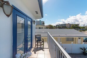 Ein Balkon mit einem Sessel und einer Pflanze im Topf, mit Blick auf eine Wohngegend mit Häusern.