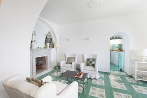 A spacious living room with a fireplace, white armchairs, a coffee table, and a view into the kitchen through an archway. - apartment a few meters from the beach (Massa Lubrense)