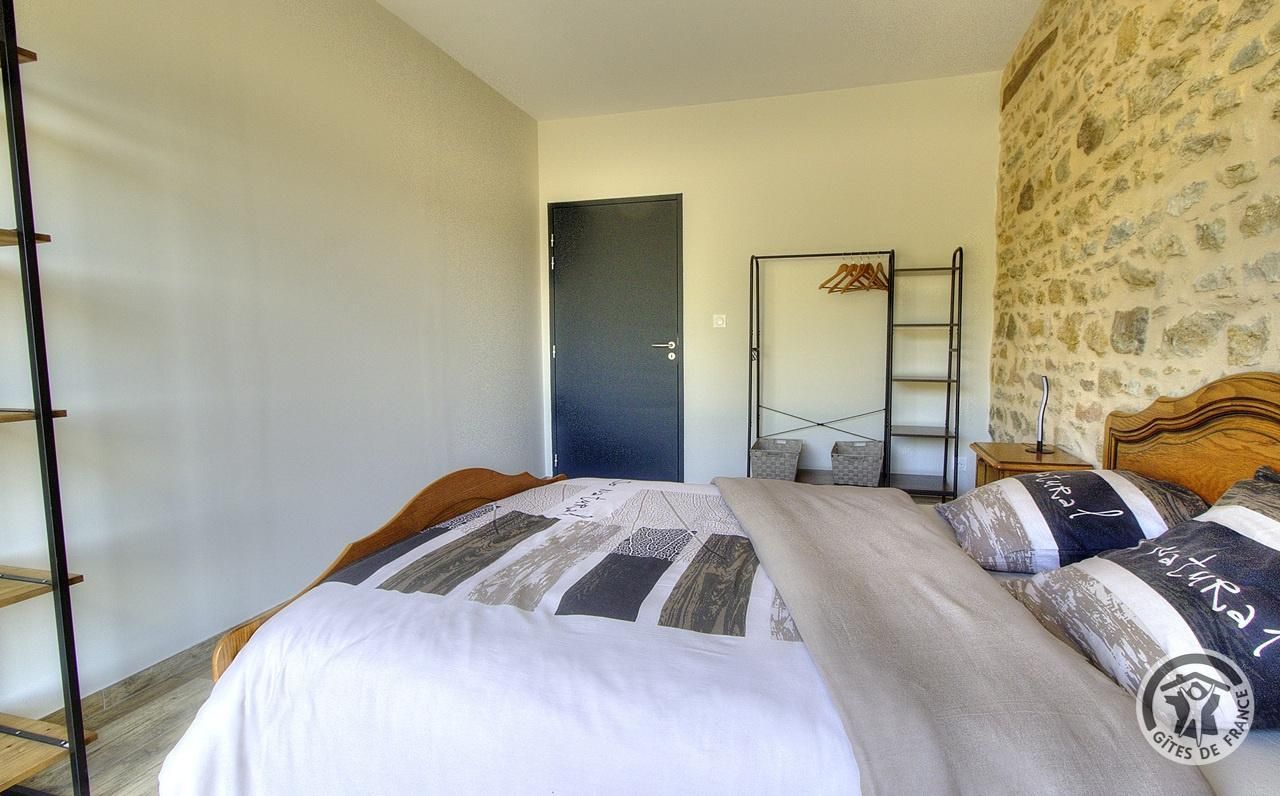 A bedroom with a bed, a wooden headboard, a wardrobe, a door, and a stone wall.