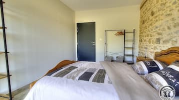 A bedroom with a bed, a wooden headboard, a wardrobe, a door, and a stone wall.