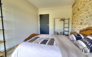 A bedroom with a bed, a wooden headboard, a wardrobe, a door, and a stone wall.
