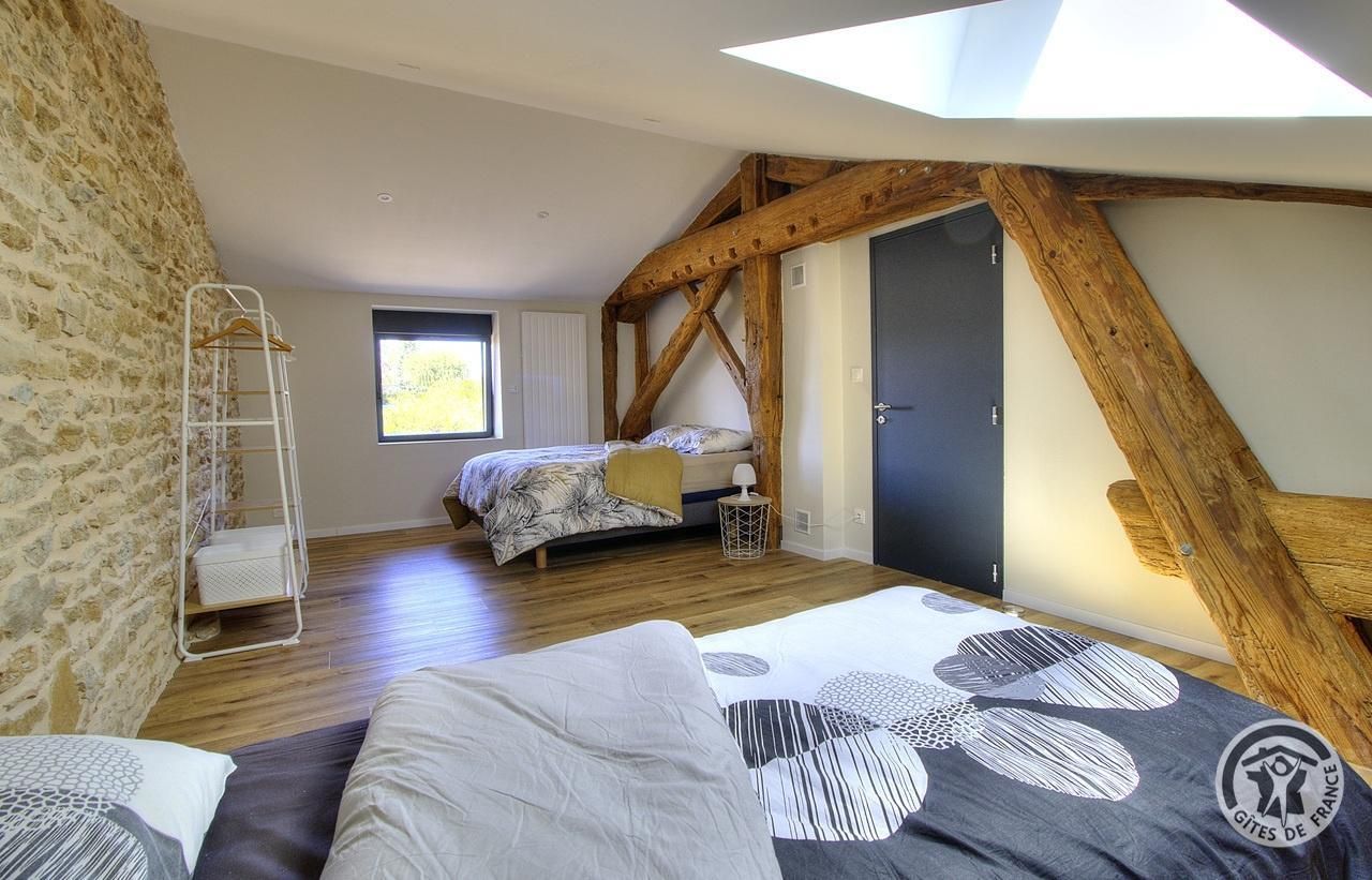 Een slaapkamer met een loft-achtige plafond, een bed met beddengoed met een patroon, een nachtkastje met een lamp en een houten ladder tegen een stenen muur.